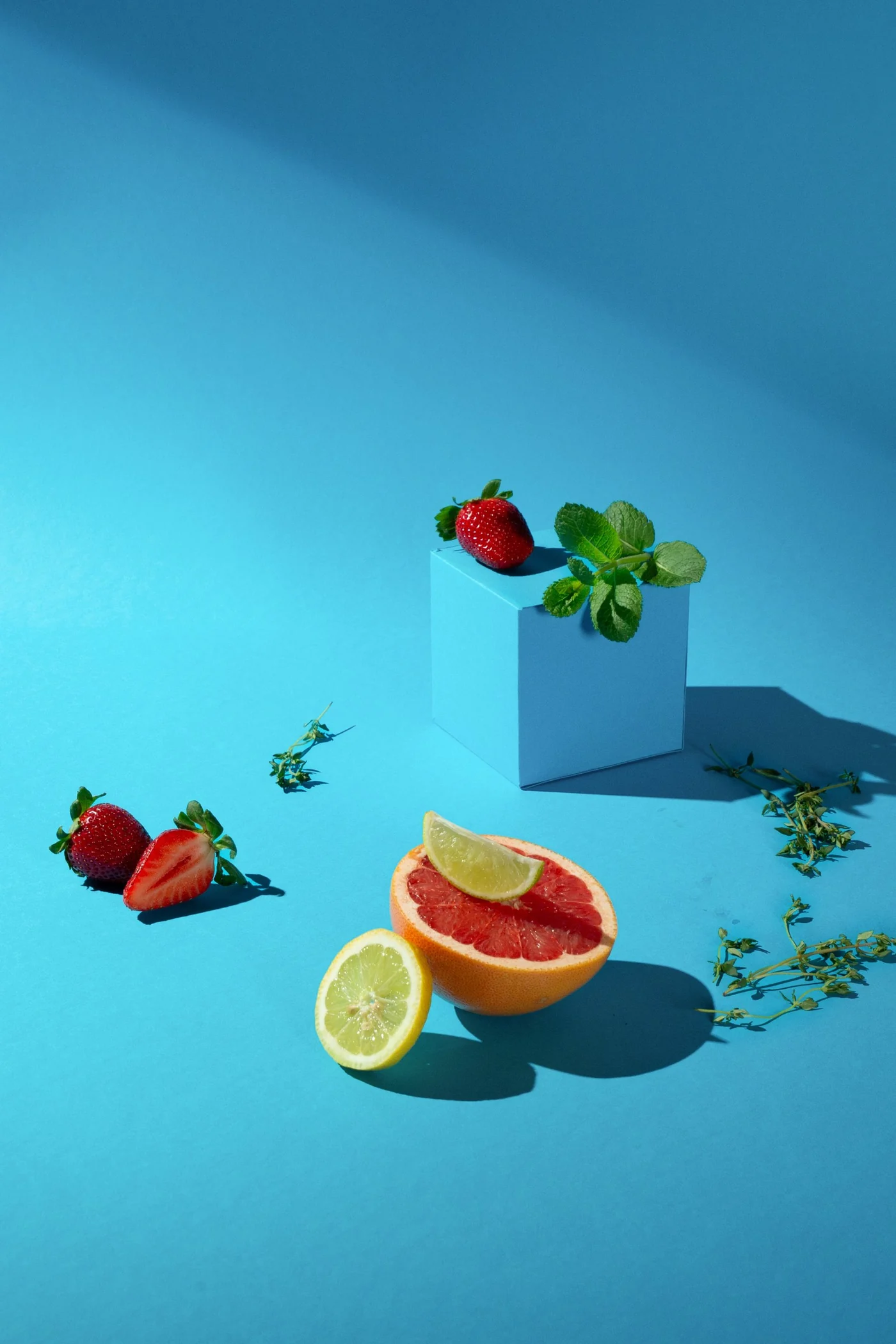 Stillleben auf blauem Grund mit Würfel, Erdbeeren, Minze, Grapefruit und Zitrone